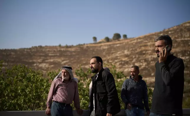 Palestinians stand on the road side after Israeli soldiers blocked access to an area for harvesting olives in the West Bank village of Sa'ir, near Hebron, Thursday, Oct. 23, 2025. (AP Photo/Leo Correa)