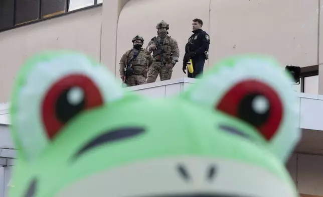 Law enforcement officers watch from a ledge of a United States Immigration and Customs Enforcement (ICE) facility as a protester stands outside in an inflatable frog costume on Tuesday, Oct. 21, 2025, in Portland, Ore. (AP Photo/Jenny Kane)