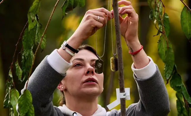 Iryna Zarytska, a widow of a fallen soldier, ties ID tags on a sakura tree as mothers and widows plant trees on a newly created Love Alley in honor of their sons and husbands who were killed in Russia-Ukraine war in Kyiv, Ukraine, Thursday, Oct. 23, 2025. (AP Photo/Efrem Lukatsky)