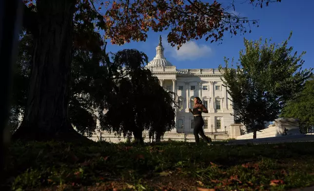 A person jogs past the U.S. Capitol amid fall foliage, Tuesday, Oct. 14, 2025, in Washington. (AP Photo/Carolyn Kaster)