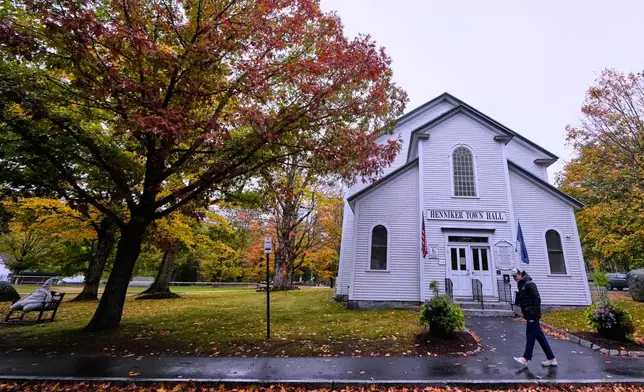 A student walks past trees with colorful fall foliage, Tuesday, Oct. 14, 2025, in Henniker, N.H. (AP Photo/Charles Krupa)