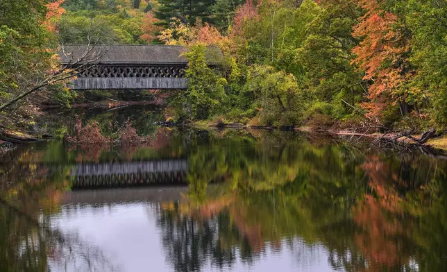 Trees with colorful fall foliage line the banks of the Contoocook River near a covered bridge, Tuesday, Oct. 14, 2025, in Henniker, N.H. (AP Photo/Charles Krupa)