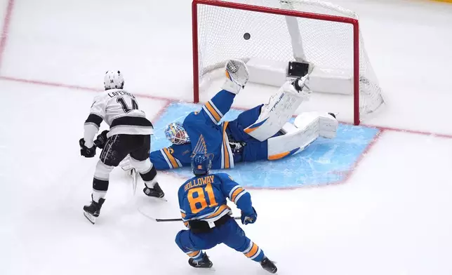 Los Angeles Kings' Alex Laferriere (14) scores past St. Louis Blues goaltender Jordan Binnington (50) as Blues' Dylan Holloway (81) watches during the second period of an NHL hockey game Tuesday, Oct. 21, 2025, in St. Louis. (AP Photo/Jeff Roberson)