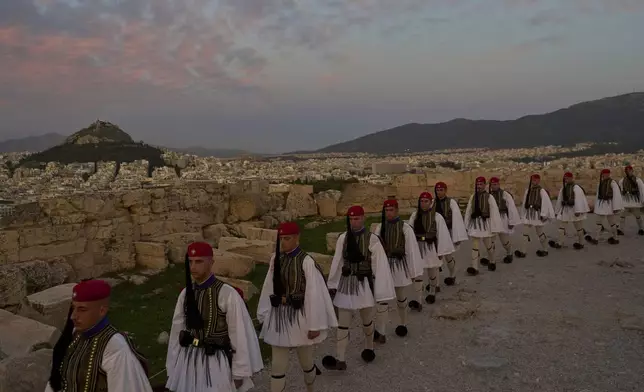 Presidential guards walk on the ancient Acropolis hill after the lowering of the Greek flag, as the city of Athens is seen in the background, on Sunday, Oct. 26, 2025. (AP Photo/Petros Giannakouris)