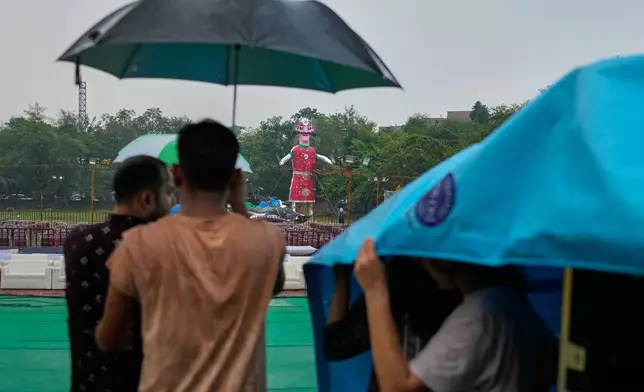 Organizers shelter under umbrellas and plastic sheeting as a sudden rain and thunderstorm causes the effigy of demon king Ravan and others to fall and sustain water damage during the Hindu festival of Dussehra in New Delhi, India, Thursday, Oct. 2, 2025. (AP Photo/Manish Swarup)