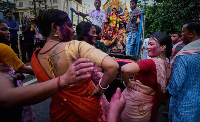 Devotees with color-smeared faces dance on a road during a procession for immersion of an idol of Hindu goddess Durga in Guwahati, Thursday, Oct. 2, 2025. (AP Photo/Anupam Nath)