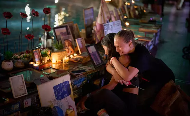 Yuval Miranda and Katya Emelianova cry as they embrace next to the photographs of Israelis who were killed in the deadly Oct. 7, 2023 Hamas attack on Israel, at a memorial marking the two year anniversary of the assault, in Tel Aviv, Israel, Tuesday, Oct. 7, 2025. (AP Photo/Emilio Morenatti)