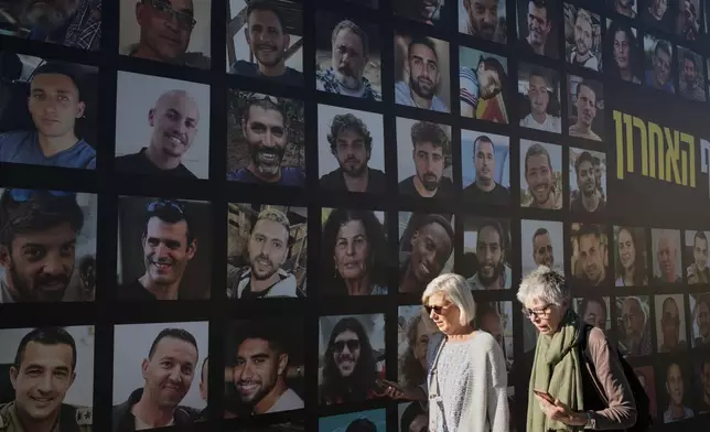 Women walk past a banner with photographs of hostages who were kidnapped and held by Hamas in the Gaza Strip, in Jerusalem, Tuesday, Oct. 7, 2025, on the second anniversary of Hamas' cross-border attack on Israel on Oct. 7, 2023, which sparked the ongoing war in Gaza. (AP Photo/Leo Correa)