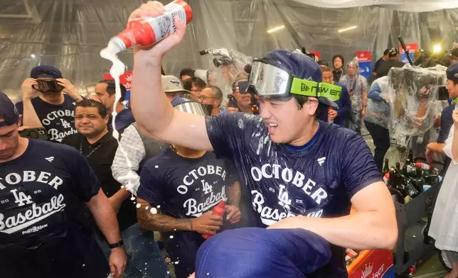 Los Angeles Dodgers' Shohei Ohtani, right, celebrates in the clubhouse after a win over the Cincinnati Reds in Game 2 of the National League Wild Card baseball playoff series Wednesday, Oct. 1, 2025, in Los Angeles. (AP Photo/Mark J. Terrill)