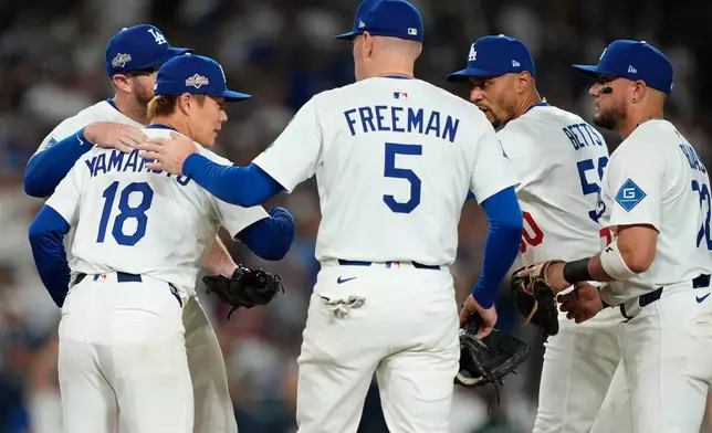 Los Angeles Dodgers starting pitcher Yoshinobu Yamamoto is hugged by teammates as he is relieved during the seventh inning in Game 2 of the National League Wild Card baseball playoff series against the Cincinnati Reds, Wednesday, Oct. 1, 2025, in Los Angeles. (AP Photo/Mark J. Terrill)