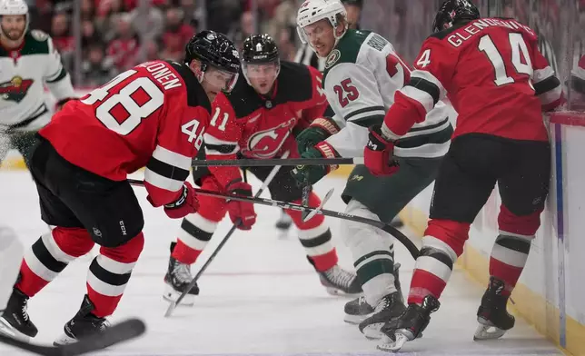 Minnesota Wild's Jonas Brodin (25), second from right, tries to get the puck past New Jersey Devils' Brian Halonen, left, and Luke Glendening, right, during the first period of an NHL hockey game Wednesday, Oct. 22, 2025, in Newark, N.J. (AP Photo/Seth Wenig)