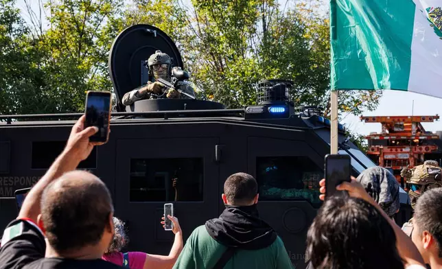 An ICE officer watches protestors as a Lenco BearCat vehicle drives to the scene in the Brighton Park neighborhood of Chicago, on Saturday, Oct. 4, 2025, after protesters learned that U.S. Border Patrol shot a woman Saturday morning on Chicago's Southwest Side. (Anthony Vazquez/Chicago Sun-Times via AP)