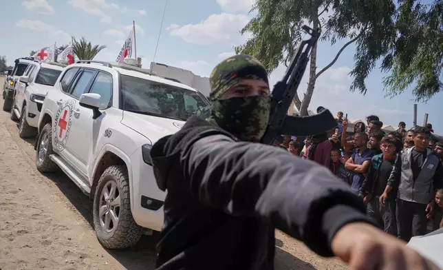 ICRC vehicles carrying released Israeli hostages make their way through groups of Palestinians and Hamas gunmen on their way to the Israeli border, in Khan Younis, southern Gaza Strip, Monday, Oct. 13, 2025. (AP Photo/Jehad Alshrafi)
