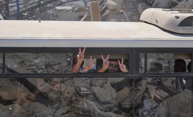 Freed Palestinian prisoners on a bus flash the victory sign as they pass destroyed buildings in the Gaza Strip after their release from Israeli jails under a ceasefire agreement between Hamas and Israel, in Khan Younis, southern Gaza Strip, Monday, Oct. 13, 2025. (AP Photo/Jehad Alshrafi)