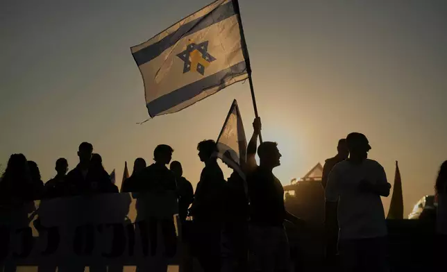 People hold Israeli flags as they gather before the release of Israeli hostages held in Gaza, outside a military base near Reim, southern Israel, on Monday, Oct. 13, 2025. (AP Photo/Leo Correa)