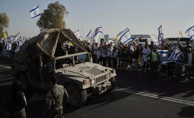 People wave Israeli flags as a military vehicle passes before the arrival of a convoy carrying hostages released from the Gaza Strip at a military base near Reim, southern Israel, Monday, Oct. 13, 2025. (AP Photo/Leo Correa)