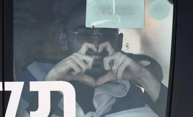 Rom Breslavski, an Israeli hostage released from the Gaza Strip smiles making a heart sign from a minibus at the Sheba Medical Center in Ramat Gan, Israel, Monday, Oct. 13, 2025. (AP Photo/Leo Correa)