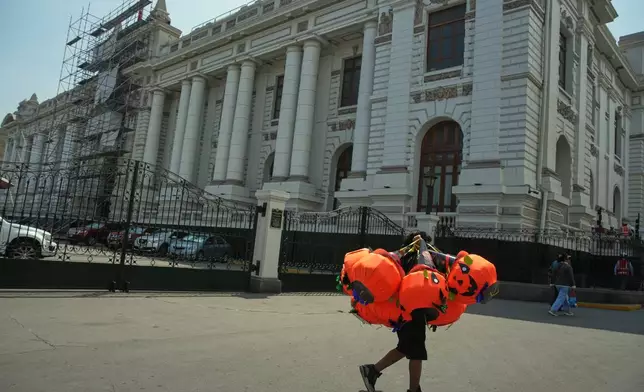 A vendor carries Halloween-themed pumpkin piñatas past Congress in Lima, Peru, Friday, Oct. 10, 2025, the day lawmakers voted to remove President Dina Boluarte from office. (AP Photo/Guadalupe Pardo)