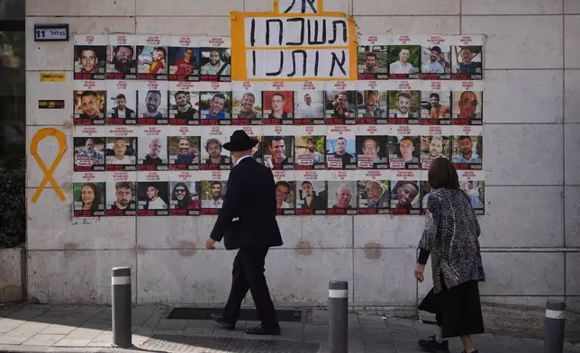 People look at photos of hostages held by Hamas in Gaza, in Jerusalem, Saturday, Oct. 4, 2025. Hebrew sign reads, "don't forget us". (AP Photo/Ohad Zwigenberg)