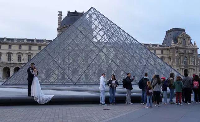 A wedding couple hugs as visitors queue to enter the Louvre museum three days after historic jewels were stolen in a daring daylight heist, Wednesday, Oct. 22, 2025 in Paris. (AP Photo/Thibault Camus)