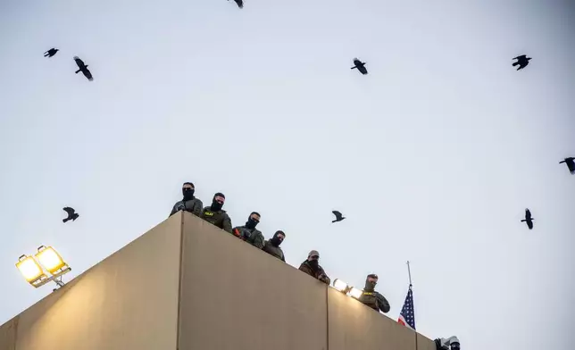 Police and federal officers stand guard on the roof of the U.S. Immigration and Customs Enforcement facility in Portland, Ore., Sunday, Oct. 5, 2025. (AP Photo/Ethan Swope)