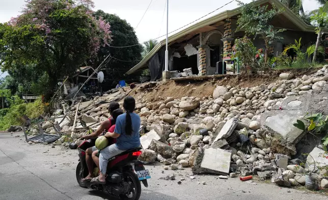 Motorists move past a house that was damaged by a strong earthquake in Manay town, Davao Oriental province, southern Philippines Saturday, Oct. 11, 2025. (AP Photo/Jeoffrey Maitem)