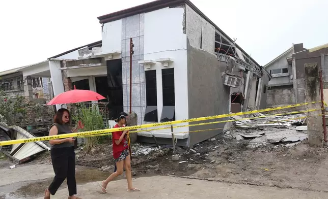 Two women walk past a damaged house after a strong earthquake in Davao City, southern Philippines on Friday Oct. 10, 2025. (AP Photo/Manman Dejeto)