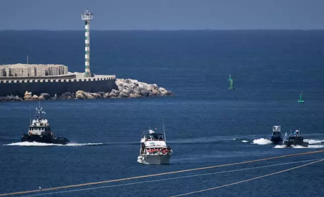 Activists in orange life jackets sit aboard a Gaza-bound Sumud flotilla boat as Israeli navy soldiers sail it into the port of Ashdod, Israel, Thursday, Oct. 2, 2025, after it was intercepted while approaching the Gaza coast. (AP Photo/Leo Correa)