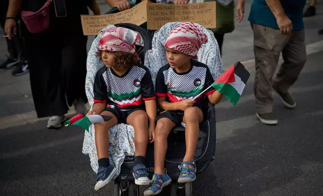 Two children sit in their stroller with a sign reading in Catalan: "Netanyahu is so bad that even the Three Wise Men won't bring him coal." during a pro-Palestinian rally in solidarity with the Global Sumud Flotilla after ships were intercepted by the Israeli navy, in Barcelona, Spain, Saturday, Oct. 4, 2025. (AP Photo/Emilio Morenatti)