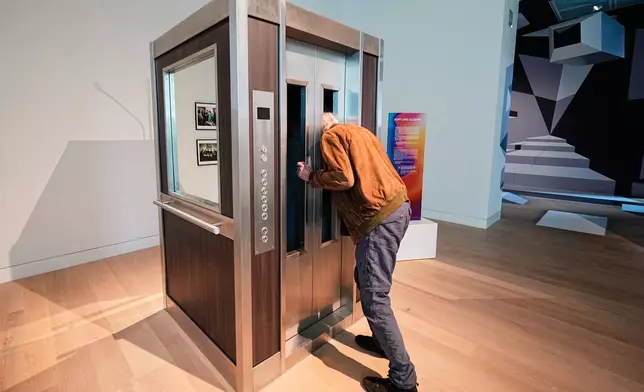 A man puts his head into an elevator where he smells a scent based on samples that NASA collected at space during the exhibition "The Secret Power of Scents", showing the history of scent from antiquity to the present as a sensory experience at the Kunstpalast art museum in Duesseldorf, Germany, Tuesday, Oct. 28, 2025. (AP Photo/Martin Meissner)