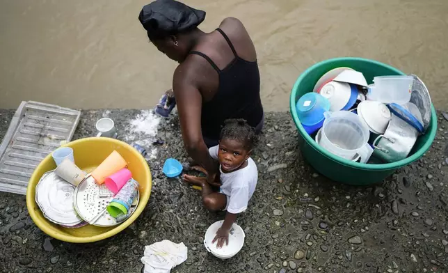 FILE - A mother and her baby wash dishes in the Atrato River, in El Arenal, Colombia, Sept. 26, 2024. (AP Photo/Ivan Valencia, File)