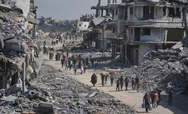 Displaced Palestinians walk with their belongings past destroyed buildings as they return to their homes in Khan Younis, southern Gaza Strip, Friday, Oct. 10, 2025, after Israel and Hamas agreed to a pause in their war and the release of the remaining hostages. (AP Photo/Jehad Alshrafi)