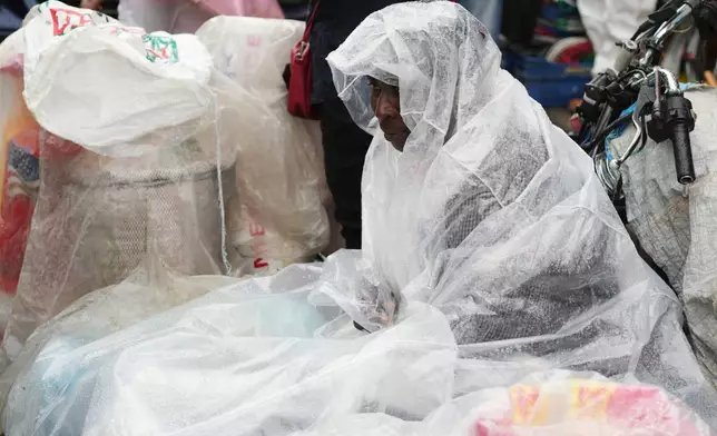 A street vendor covers up in plastic during a light rain in the Petion-Ville neighborhood of Port-au-Prince, Haiti, Tuesday, Oct. 28, 2025, as Hurricane Melissa passes through the Caribbean. (AP Photo/Odelyn Joseph)