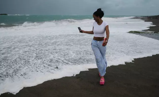 A woman strolls along the beach ahead of the forecast arrival of Hurricane Melissa in Kingston, Jamaica, Sunday, Oct. 26, 2025. (AP Photo/Matias Delacroix)