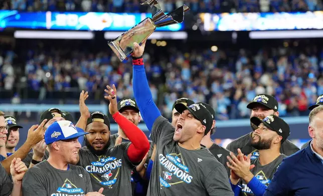 Toronto Blue Jays' George Springer holds the American League Championship Series trophy as the team celebrates after defeating the Seattle Mariners in Game 7 of the series in Toronto, Monday, Oct. 20, 2025. (Frank Gunn/The Canadian Press via AP)