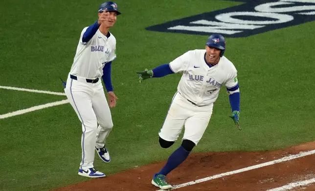 Toronto Blue Jays first base coach Mark Budzinski, left, cheers on George Springer, right, who rounds the bases after hitting a three-run home run against the Seattle Mariners during the seventh inning in Game 7 of baseball's American League Championship Series in Toronto, Monday, Oct. 20, 2025. (Chris Young/The Canadian Press via AP)
