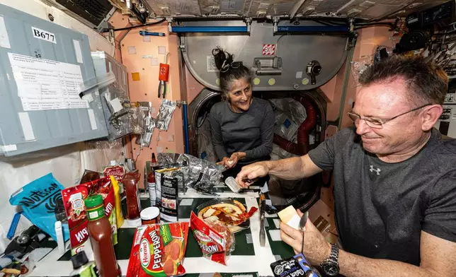 FILE - In this photo provided by NASA, astronauts Suni Williams and Butch Wilmore, both Expedition 71 flight engineers, make pizza aboard the International Space Station's galley located inside the Unity module on Sept. 9, 2024. Items are attached to the galley using tape and velcro to keep them from flying away in the microgravity environment. (NASA via AP, File)