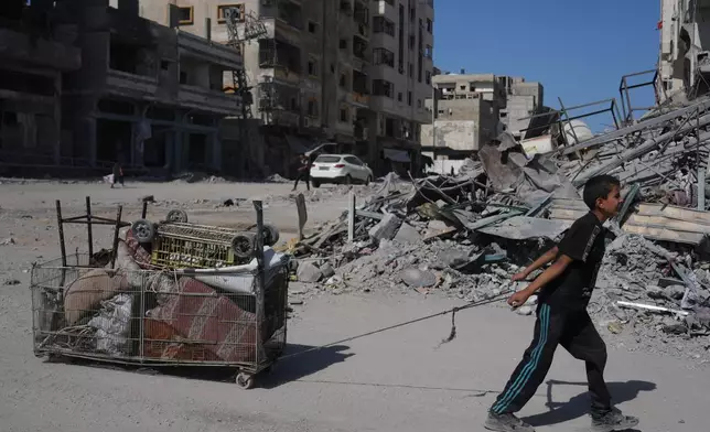 A displaced Palestinian boy pulls a cart loaded with belongings as he walks along the heavily damaged Al-Jalaa Street in Gaza City, Saturday, Oct. 11, 2025, after Israel and Hamas agreed to a pause in their war and the release of the remaining hostages. (AP Photo/Abdel Kareem Hana)
