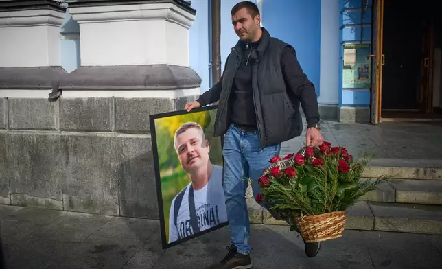 A man caries a photo of cameraman Yevhen Karmazin, who was killed together with corespondent Olena Hubanova, who worked under the pseudonym Alyona Gramova on Thursday, Oct. 23, when a Russian Lancet drone hit their vehicle in Ukraine's Kramatorsk around 20 kilometres from the front line, after funeral service at St. Michael Monastery in Kyiv, Ukraine, Monday, Oct. 27, 2025. (AP Photo/Efrem Lukatsky)