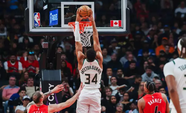 Milwaukee Bucks' Giannis Antetokounmpo (34) dunks while Toronto Raptors' Sandro Mamukelashvili (54) and Scottie Barnes (4) look on during first half NBA basketball action in Toronto on Friday, Oct. 24, 2025. (Nick Iwanyshyn/The Canadian Press via AP)