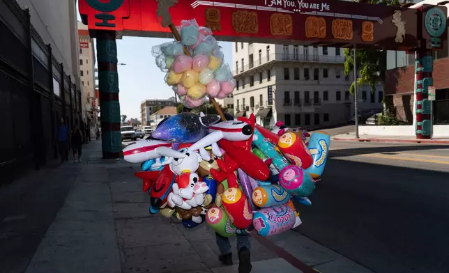 FILE - A street vendor carries cotton candy and inflatable toys near MacArthur Park in Los Angeles, an area targeted in recent ICE raids, on July 19, 2025. (AP Photo/Jae C. Hong, File)