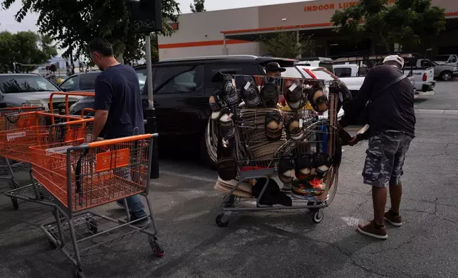 FILE - Vendor Felix, right, shows merchandise to a man as a shopper returns a cart in the parking lot of a Home Depot in the Van Nuys section of Los Angeles, Aug. 28, 2025. (AP Photo/Jae C. Hong, File)