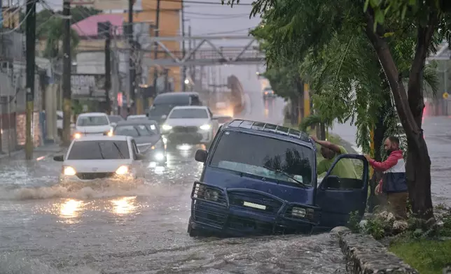 People abandon a car on an impassable street flooded by rains caused by Tropical Storm Melissa in Santo Domingo, Dominican Republic, Friday, Oct. 24, 2025. (AP Photo/Ricardo Hernandez)