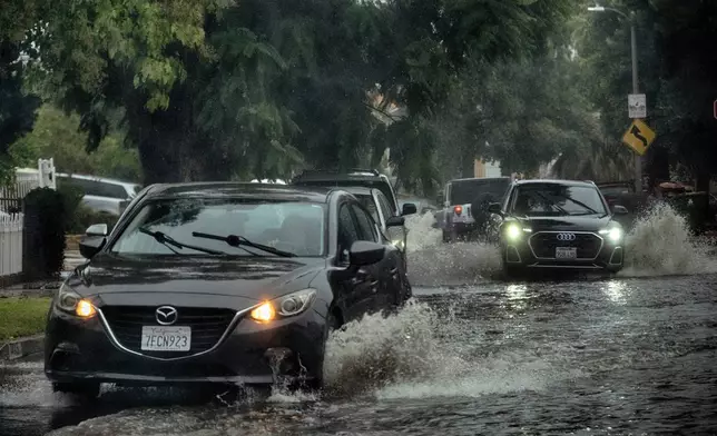 Morning commuters maneuver a flooded street during a flash flood warning in the San Fernando Valley section of Los Angeles on Tuesday, Oct. 14, 2025. (AP Photo/Richard Vogel)
