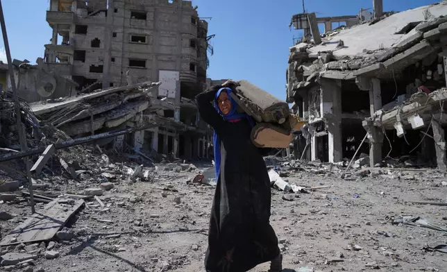 An elderly displaced Palestinian woman carries an item past destroyed buildings in Khan Younis, southern Gaza Strip, Friday, Oct. 10, 2025, after Israel and Hamas agreed to a pause in their war and the release of the remaining hostages. (AP Photo/Jehad Alshrafi)