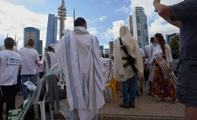 Covered in prayer shawls, men pray and hold the four items used as a symbol on the Jewish holiday of Sukkot, at a plaza known as hostages square following the announcement that Israel and Hamas have agreed to the first phase of a peace plan to pause the fighting in Gaza, in Tel Aviv, Israel, Friday, Oct. 10, 2025. (AP Photo/Ariel Schalit)