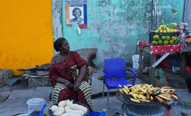 A street vendor sells under a campaign poster of presidential candidate Simone Gbagbo in Abidjan, Ivory Coast, Tuesday, Oct. 22, 2025. (AP Photo/Misper Apawu)