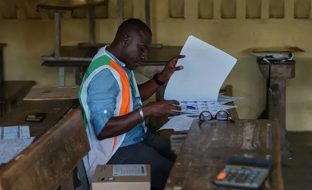 An election official looks through a voter register at a polling station in Yopougon during the presidential elections in Abidjan, Ivory Coast, Saturday, Oct. 25, 2025. (AP Photo/Misper Apawu)