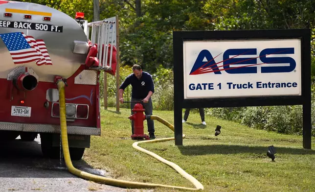 A person attaches a hose to a fire hydrant to fill a tanker truck after a blast resulted in multiple fatalities and others missing at Accurate Energetic Systems, an explosives plant, Friday, Oct. 10, 2025, in Bucksnort, Tenn. (AP Photo/John Amis)
