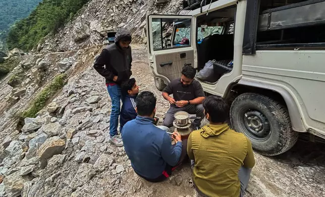 Travelers make tea as they wait for a mountain road to be cleared of debris near Laspa village, in the northern Indian Himalayan state of Uttarakhand, on Oct. 4, 2025. (AP Photo/Satish Sharma)